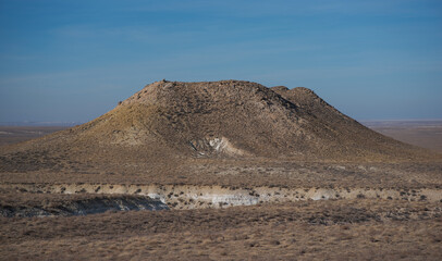 A solitary hill surrounded by vast arid plains under a clear blue sky, showcasing a serene and rugged desert landscape in a remote wilderness location.