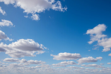 Vibrant blue sky with a dynamic array of fluffy white cumulus clouds, signifying changing weather patterns and natural beauty.