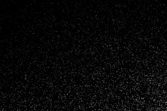 Black and white abstract image resembling snowfall at night or a starry sky, with countless white specks scattered across a dark background.