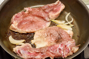 Marinated meat is fried with onions and vegetable oil in a frying pan.