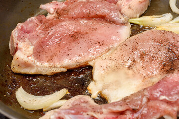 A close-up of marinated meat being fried with onions and vegetable oil in a frying pan.