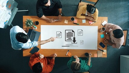 A diverse team collaborates on project planning in a modern office, surrounded by laptops and documents on a wooden table, fostering innovative ideas and teamwork. Raster