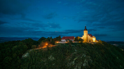 Kirche auf dem Hügel mit beleuchtetem Glockenturm und Himmel bei Nacht
