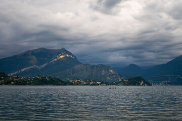 Stormy skies above the tranquil lake as a small boat navigates the calm waters at dusk near the mountains