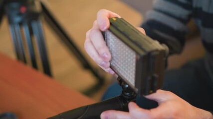 Lighting operator adjusts led light fixture on tripod in studio setting. Focused on proper setup for shoot, ensuring quality lighting for professional filming