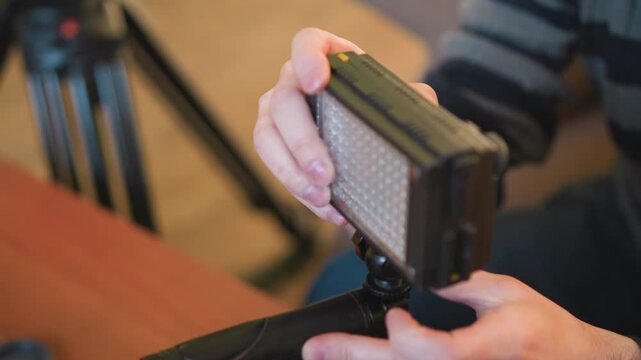Lighting operator adjusts led light fixture on tripod in studio setting. Focused on proper setup for shoot, ensuring quality lighting for professional filming