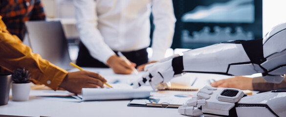 A futuristic office scene showcasing collaboration between human workers and a robotic arm, highlighting innovative technology and data analysis for business growth.Noogenesis