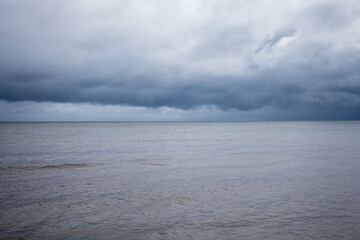 Dark clouds gather over the calm sea on a quiet afternoon, creating a serene yet dramatic atmosphere in the coastal landscape