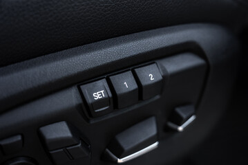 Close up view of seat adjustment controls in a BMW X6, featuring preset buttons labeled SET, 1, and 2, with a black textured finish surrounding them. © Aerial Film Studio
