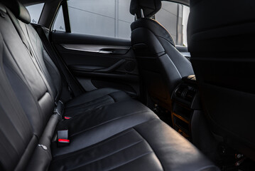 Close up of the BMW X6 rear passenger area showing black leather seats with stitching, metallic door accents, and rear air vents in an urban setting. © Aerial Film Studio