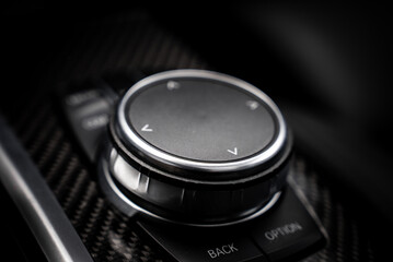 Detailed view of the BMW X4 iDrive controller, featuring a circular knob, metallic trim, carbon fiber surface, and labeled buttons for functionality. © Aerial Film Studio