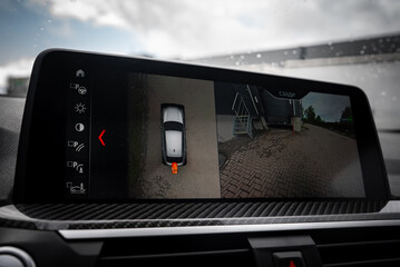 Close up of BMW X4 interior display with parking assist system, showing top down and rear camera views, carbon fiber trim, and raindrops on windshield.
