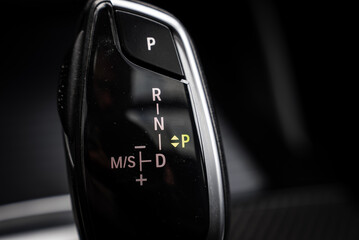 Close up view of the BMW X4 gear selector, featuring glossy black and chrome details, illuminated markings, and a blurred background for emphasis. © Aerial Film Studio