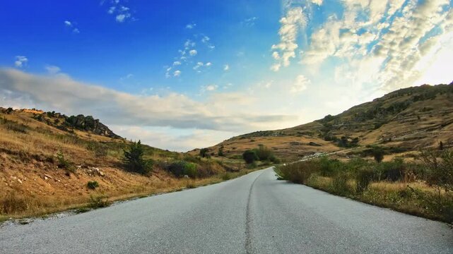 POV Joyride on local road across uneven terrain, golden meadows, blue sky clouds