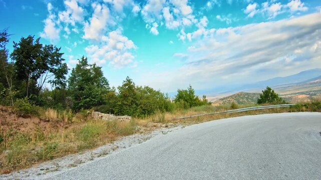 POV drive downhill, rocks, green trees and dry grass, blue sky clouds