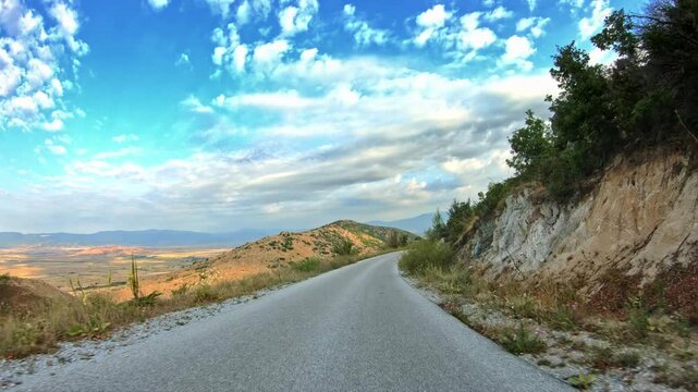 High terrain curvy road, POV car driving, dry vegetation, blue sky clouds