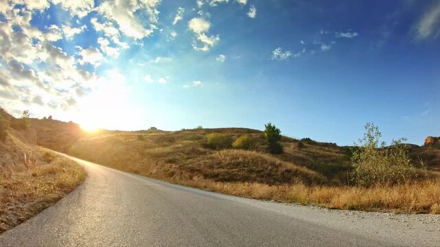 Upward the local curvy mountain road, shining sun, blue sky clouds, POV drive