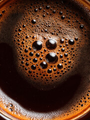 Dark coffee surface with bubbles reflecting light in a warm cup