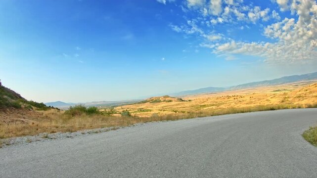 Nature, fluffy clouds blue sky, golden slopes, POV drive descending local road