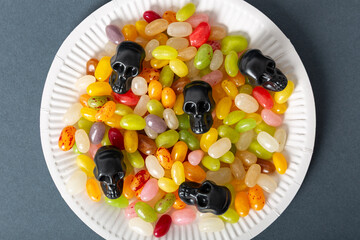 Halloween candy skulls and jelly beans on a white plate on a dark background, close-up