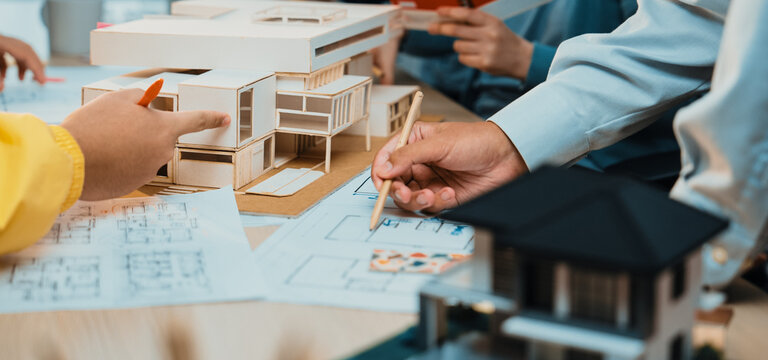 A dynamic architecture design session featuring scale models and blueprints spread across a collaborative workspace table. Focus on teamwork and creativity. SACTR