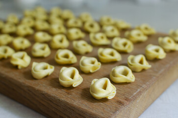 Raw homemade tortellini on a wooden cutting board on a gray background. Traditional Italian food concept. Selective focus. Horizontal orientation.