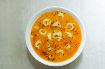 Tortellini soup with chicken and parmesan in a white bowl on a gray background. Traditional Italian food concept. Selective focus. Horizontal orientation. Top view.