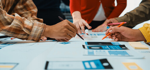 A diverse team gathers around a table filled with colorful sketches and tools, engaged in user interface design. The atmosphere is collaborative and innovative. SACTR