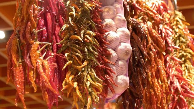 Strands of red chili peppers and garlic hang at a vibrant market stall