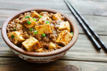 Mapo tofu dish in spicy sauce with minced beef in a ceramic bowl on a wooden background. Dish from Sichuan province. Traditional Asian food. Selective focus. Horizontal orientation.