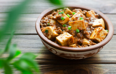 Mapo tofu dish in spicy sauce with minced beef in a ceramic bowl on a wooden background. Dish from Sichuan province. Traditional Asian food. Selective focus. Horizontal orientation.