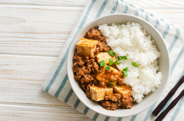 Mapo tofu dish in spicy sauce with minced beef in a ceramic bowl on a white background. Dish from Sichuan province. Traditional Asian food concept. Selective focus. Horizontal orientation. Top view.
