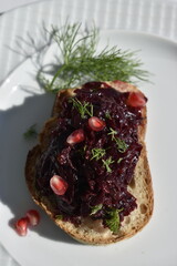 Closeup open sandwich of rye bread with beetroot spread and pomegranate seeds on a white plate