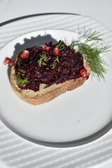 open sandwich of rye bread with beetroot spread and pomegranate seeds on a white plate, top view