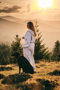 A woman and her black dog enjoy a serene sunset in the mountains. Captured in a peaceful moment, highlighting nature, companionship and tranquility. Perfect for travel and lifestyle themes.