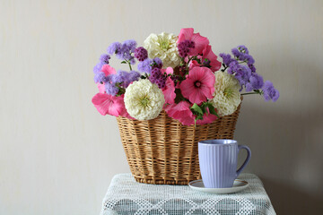 Colorful flowers bouquet in wicker basket with purple mug