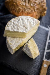 Camembert cheese on black table. French cheese with mold on the surface.