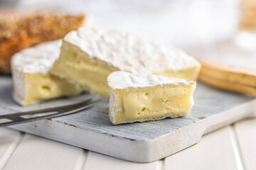 Camembert cheese on cutting board on white table. French cheese with mold on the surface.