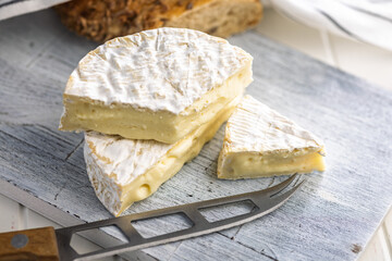 Camembert cheese on cutting board on white table. French cheese with mold on the surface.