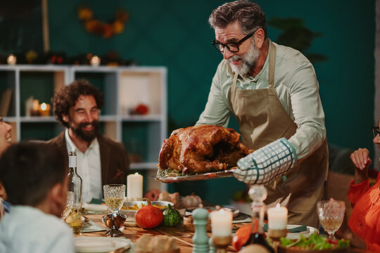 Grandfather bringing roasted turkey to thanksgiving table with family gathered around - Powered by Adobe