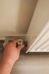  Hand turning a side valve on the radiator, adjusting water flow for proper heating. The image demonstrates manual control of home heating systems and maintenance practice. High quality photo