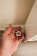 
A close-up hand holding the radiator valve knob, symbolizing control of heating and energy use. The focus is on regulation, energy saving, and household heating balance.