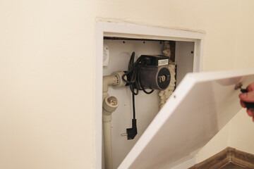 
Close view of circulation pump with wires and connected pipes inside a wall box. Heating device helps regulate water movement and maintain even temperature in the system.