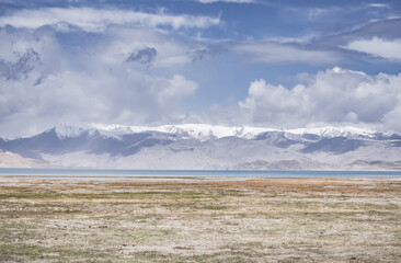 Panorama landscape of Lake Karakul in the Pamir mountains in the Tien Shan against the background of high snowy rocky peaks with clouds, morning panorama of the lake for the background