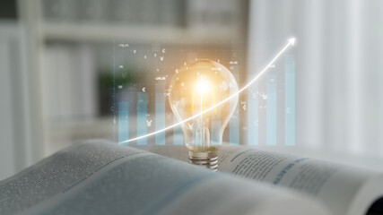 A bright light bulb glows above an open book, with a rising graph chart in the background,...