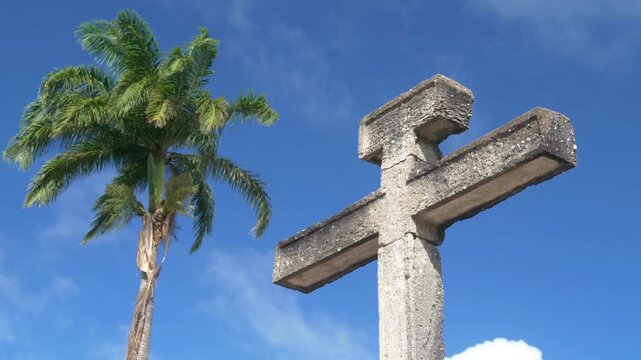 A stone cross stands tall against a vibrant blue sky with fluffy white clouds