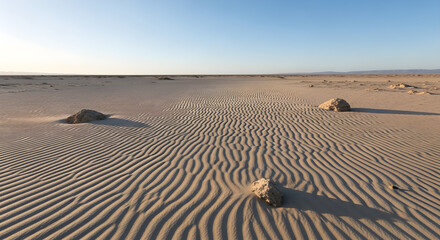 Vast Desert Landscape with Wind-Sculpted Sand Ripples and Scattered Rocks: Serene Beauty of Arid Wilderness and the Power of Natural Forces

