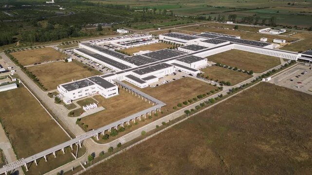 Drone aerial view of a large modern industrial manufacturing complex with warehouses, office buildings, parking areas, and landscaped grounds. Contemporary production facility located within a busines