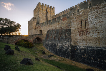 Fototapeta premium The fortified stone walls of the historic Castelo de São Jorge at sunset, showcasing medieval battlements and defensive architecture overlooking the historic city.