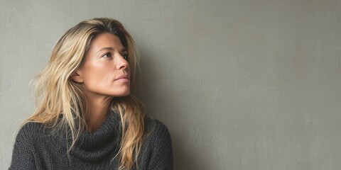 Contemplative Woman with Long Hair in a Cozy Sweater Against a Neutral Background